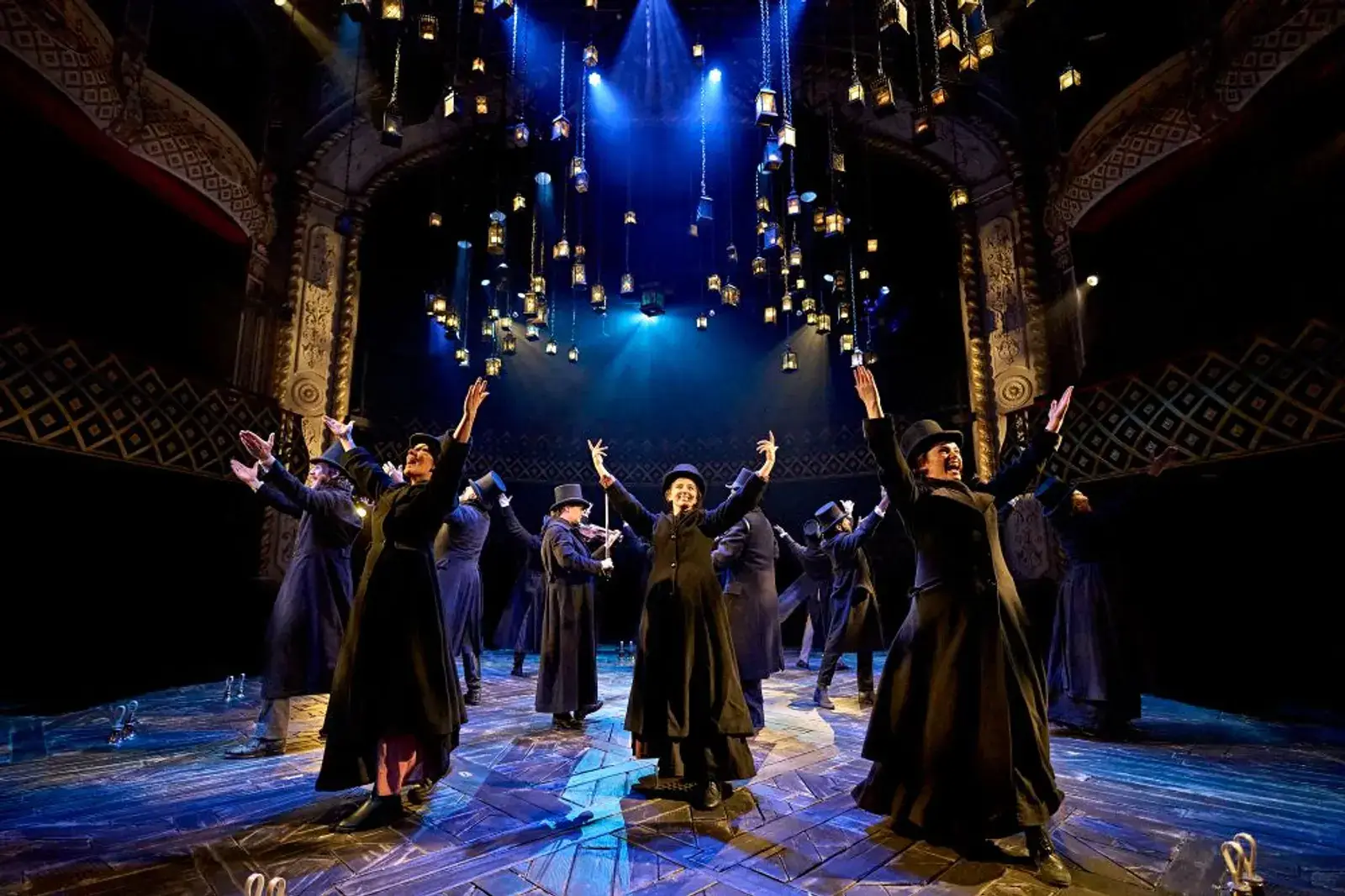 The ensemble fills the stage in Victorian dress as lanterns descend