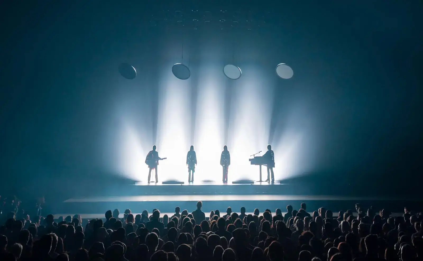 The four figures silhouetted against columns of white light