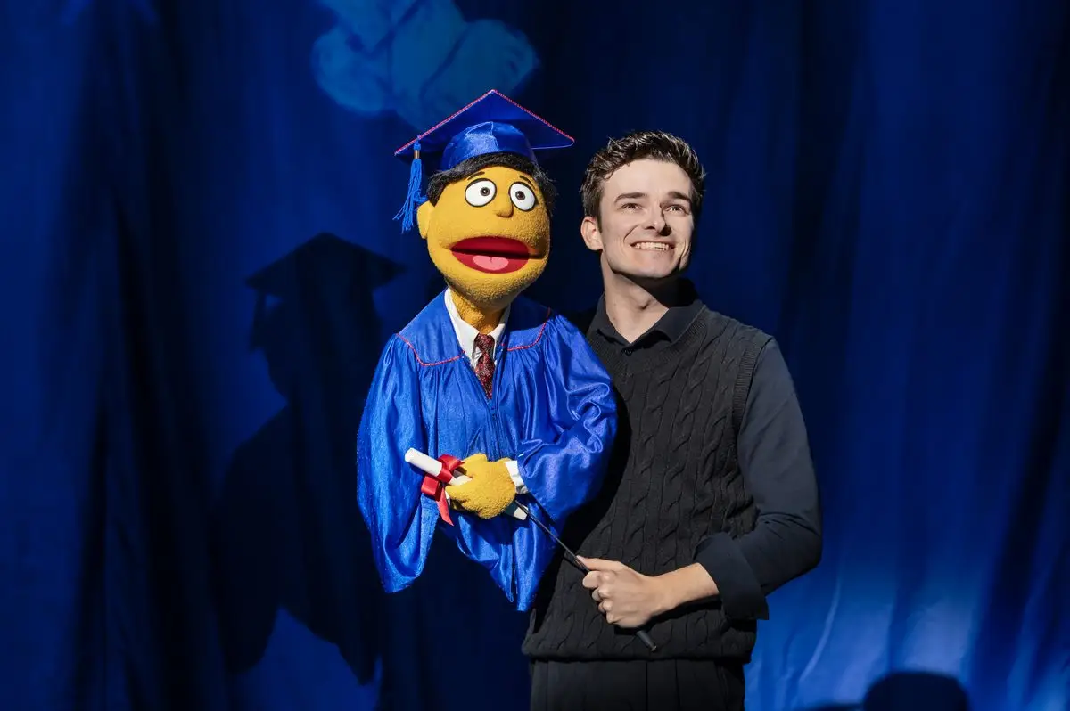 Noah Harrison with the Princeton puppet in graduation cap and gown in Avenue Q at the Shaftesbury Theatre, London