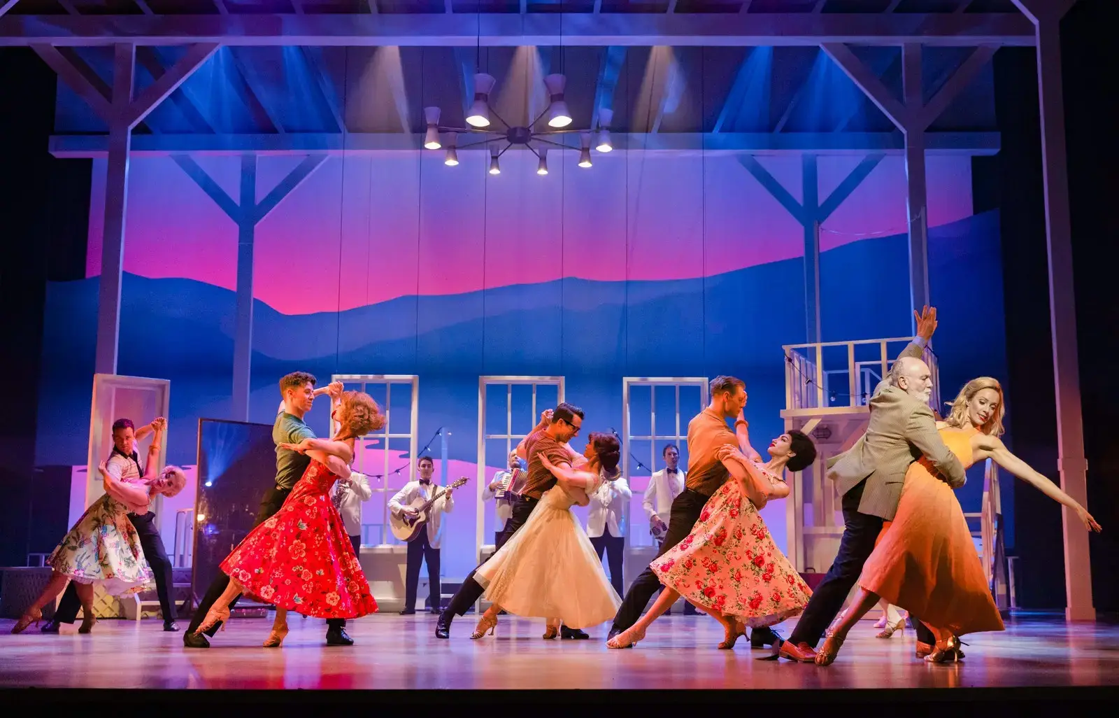 The full company in a partnered ballroom number against a mountain sunset
