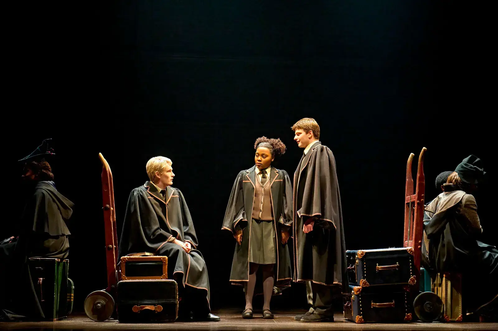 Cast in Hogwarts robes among luggage trolleys on the station platform