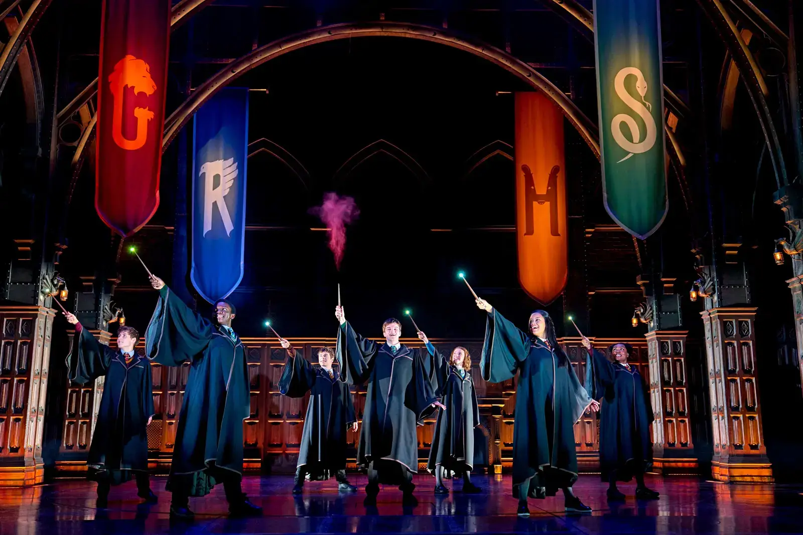 Students raise glowing wands beneath the four Hogwarts house banners