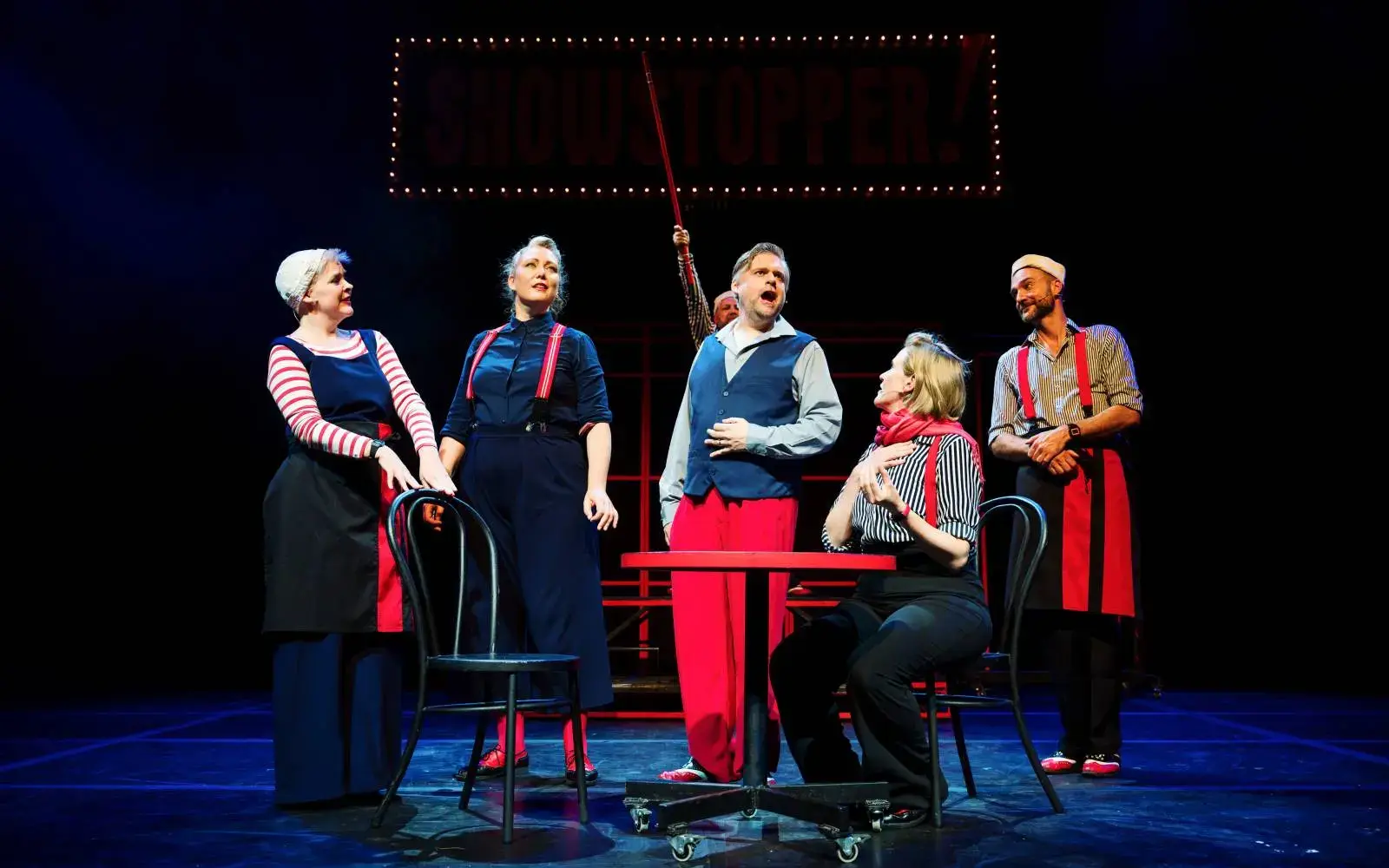 The company in a table scene beneath the marquee