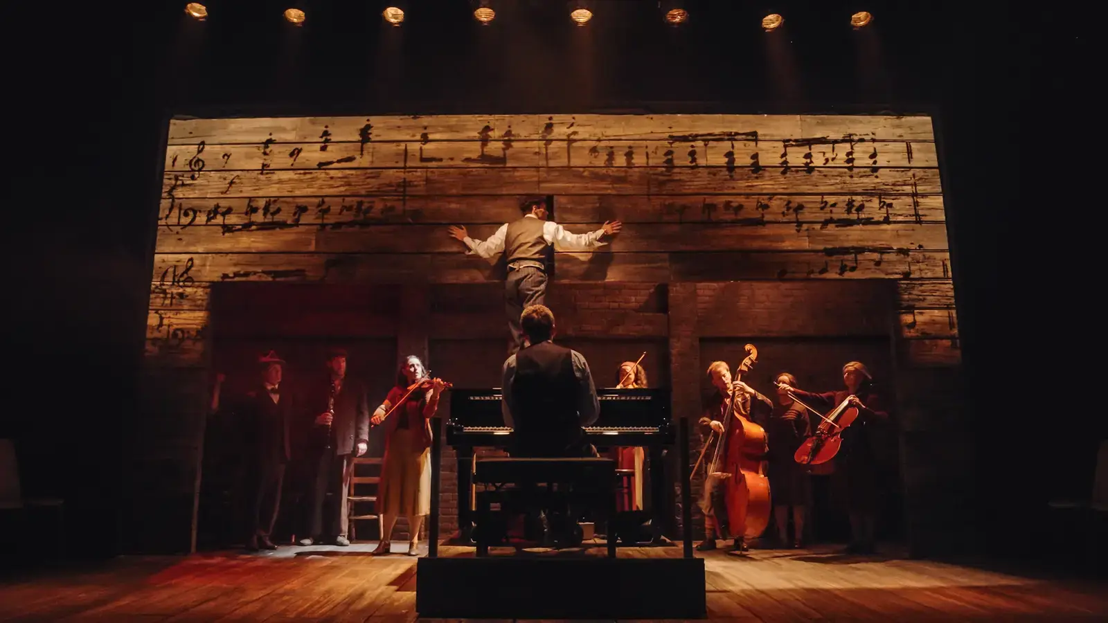 The full company before a towering wall of sheet music