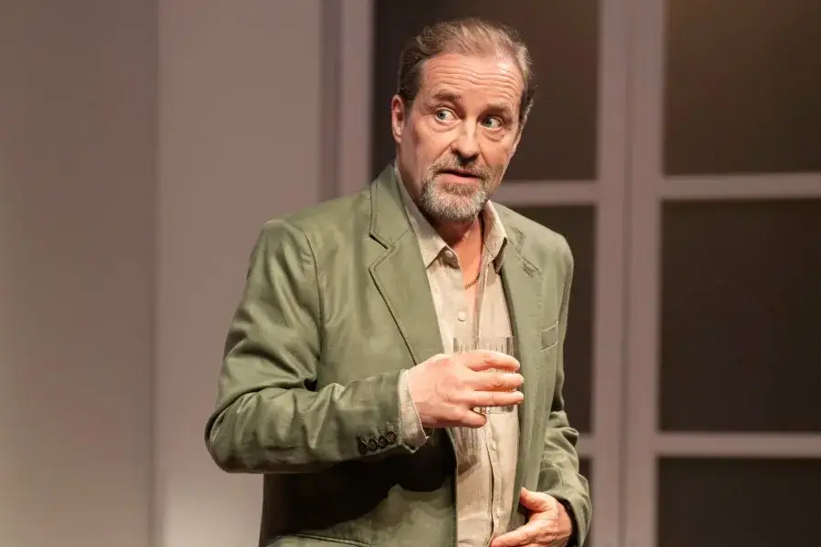 A man holding a glass mid-conversation in The Truth at the Apollo Theatre